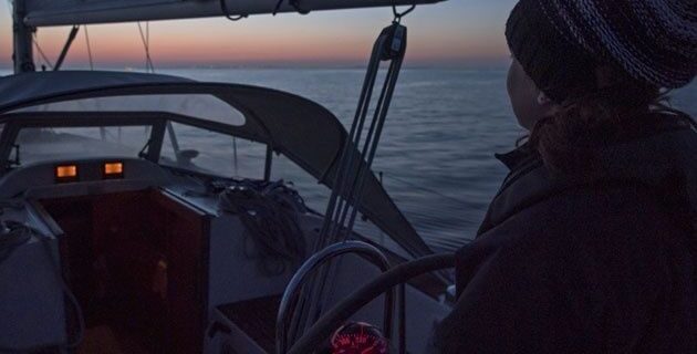 Person steuert ein Segelboot nachts mit roter Instrumentenbeleuchtung