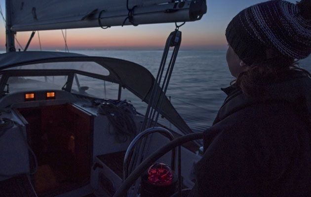 Person steuert ein Segelboot nachts mit roter Instrumentenbeleuchtung